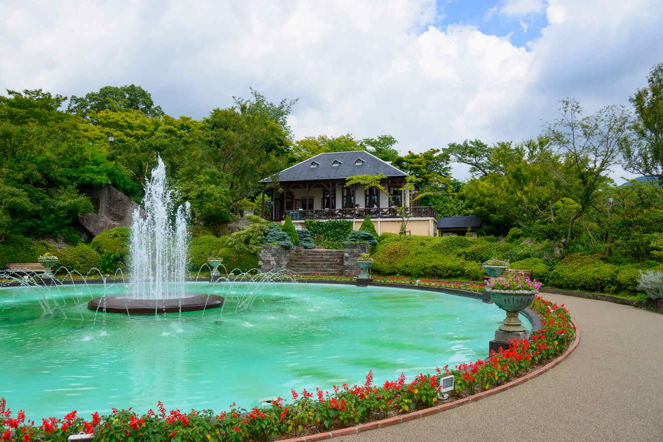 A beautifully landscaped garden with a fountain in the center, vibrant flowers, and a classic pavilion in the background